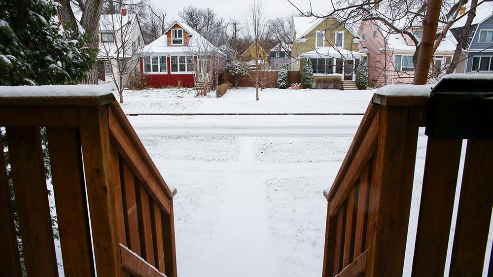 A view from a home’s front porch, looking down the steps and onto a snow-covered residential street.